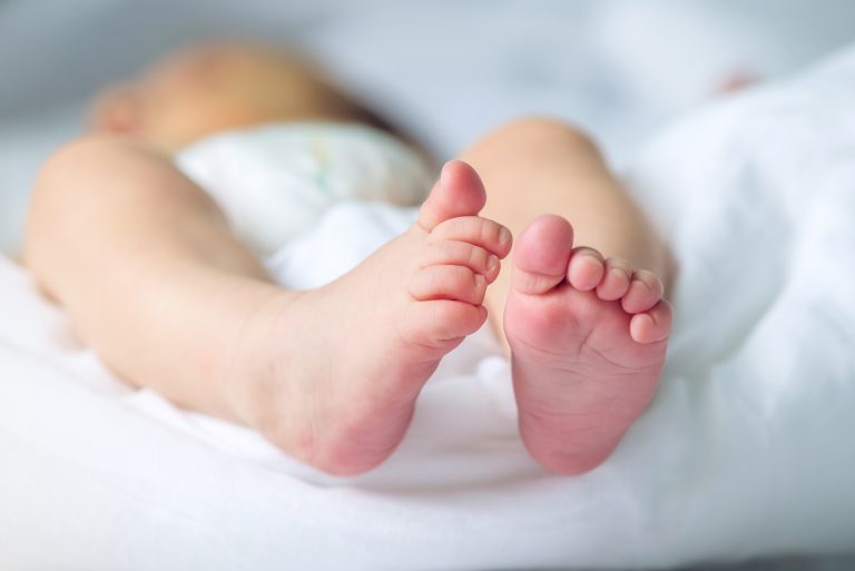 Baby feet with pink lying on a white blanket